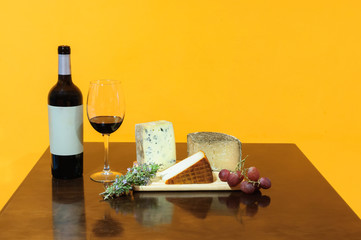 Bottle and glass of red wine, cheese board, grapes,fig and bread sticks on rustic wooden table,
