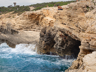 Hombre sentado encima de la cueva mirando a una mujer escalando en las rocas del Cabo de Kamenjak, en Istria, Croacia, verano de 2019