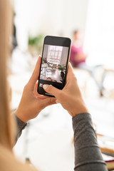 Young mobile woman with smartphone taking photo of interior of modern cafe