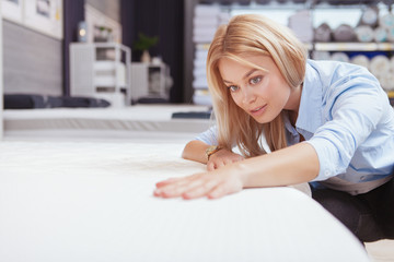 Close up of a beautiful young woman examining orthopedic mattress on sale at furnishings store