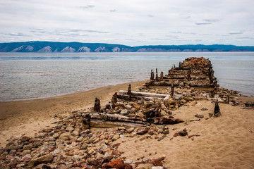 The destroyed old pier on the island of Olkhon on Lake Baikal. On the shore of stones and sand. Behind the mountain lake.