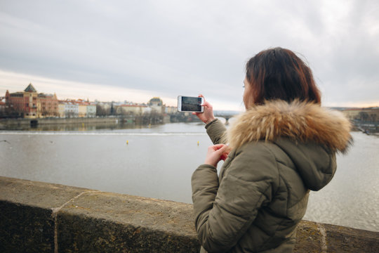 Woman is taking pictures on the Charles bridge in Prague. Young beautiful girl tourist stands on the Charles Bridge in Prague in the Czech Republic and takes photos of beautiful city views
