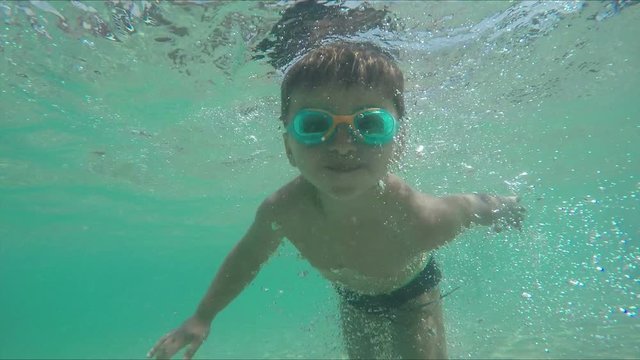 Little boy in swimming goggles learning to swim and dives under water
