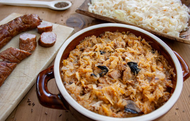 Bigos in stoneware dish and bigos ingredients: sausage, sauerkraut and cumin
