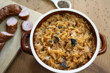 Bigos in stoneware dish and bigos ingredients: sausage, sauerkraut and cumin