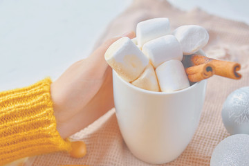 Women hand, yellow sweater and white mug. With a hot drink, marshmallow and cinnamon stick