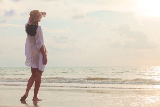 carefree woman in straw hat walking in the sunset on the beach. vacation vitality healthy living concept