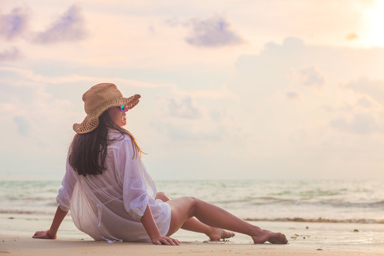 carefree woman in straw hat sitting in the sunset on the beach. vacation vitality healthy living concept