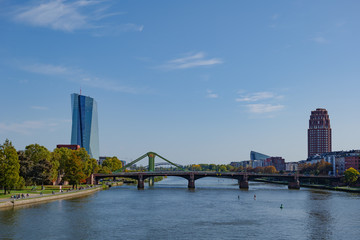Outdoor sunny view from Eiserner Steg,  Iron Bridge, of promenade on riverside of Main River and background of European Central Bank in sunny day  in Frankfurt, Germany.