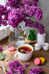 Romantic background with cup of tea, lilac flowers and macaroons. A bouquet of lilac in a vase. Floral card for Mothers or Womans Day