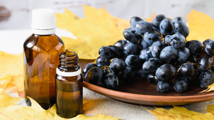 close-up, glass bottles with grape seed oil and grape berries on a plate on a white wooden table