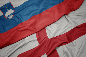 waving colorful flag of england and national flag of slovenia.