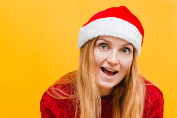 Happy excited young woman in santa claus hat over yellow background, place for text. Holiday concept.