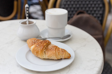 Delicious coffee with croissant. French breakfast concept. Cup of coffee on table oudoors at the cafe terrace