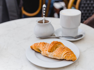 Delicious coffee with croissant. French breakfast concept. Cup of coffee on table oudoors at the cafe terrace