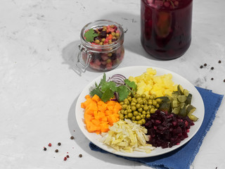 Vinaigrette ingredients are located on a plate. The plate is on a blue napkin, gray background. Near the bank with ready-made vinaigrette and beet kvass.