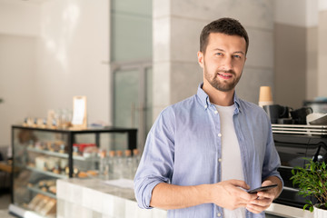 Handsome guy in casualwear scrolling in smartphone while looking at you