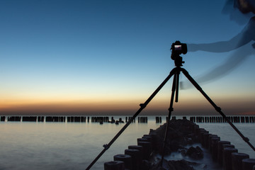 Photographer standing on the breakwater by the sea. Camera set on a tripod. sunset.