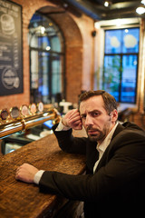 Portrait of ruffled mature businessman sitting by bar counter after work looking drunk, copy space
