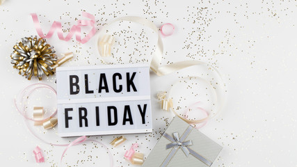 Black friday sale text on white lightbox, golden stars, holiday ribbon and box around on white background.