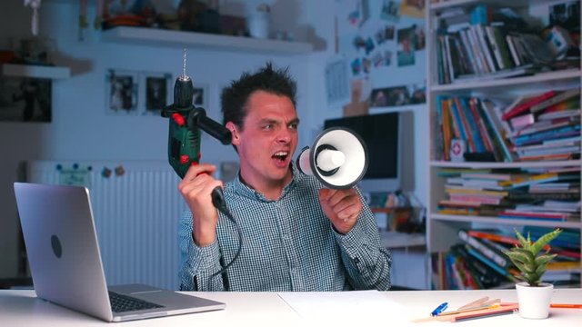 A crazy guy at the office desk shouts into a megaphone and shoots from a drill.