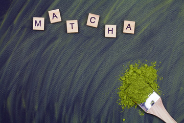 Text MATCHA and matcha green tea dry powder on brush on black background.