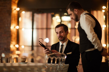 Portrait of mature bearded businessman looking at menu while ordering dinner in luxury restaurant, copy space