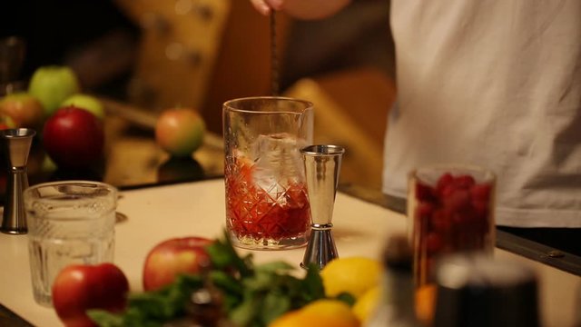 Barman stirs a thin spoon with a cocktail in a glass with ice