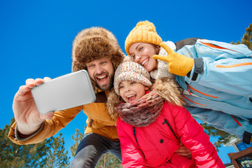 Winter vacation. Family time together outdoors taking selfie on smartphone grimacing to camera...