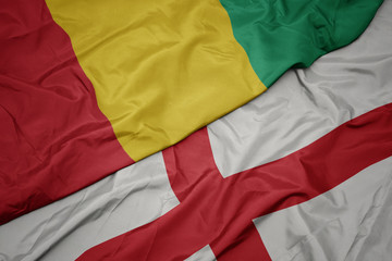 waving colorful flag of england and national flag of guinea.