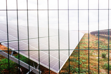 Solar panel or photovoltaic farm behind metal chainlink fence on green field with dramatic cloudy sky in North Germany
