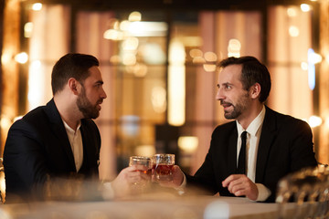 Side view portrait of two business partners drinking whiskey while enjoying dinner in luxury restaurant after work