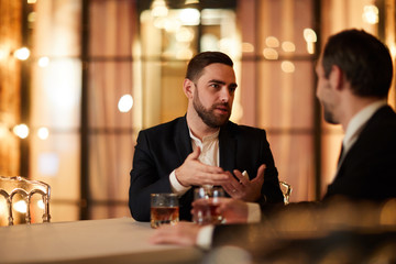 Portrait of two business people talking while sitting at table in luxury restaurant and drinking alcohol after work, copy space