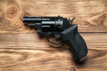 Pneumatic handgun on brown wooden board background.