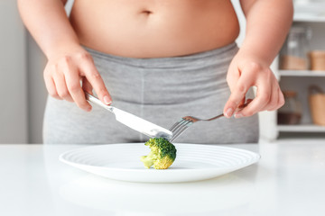 Body Care. Chubby girl with bare belly standing near kitchen table cutting broccoli close-up