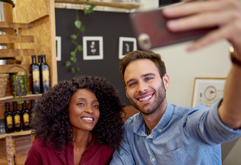 Diverse couple smiling while taking selfies together in a cafe