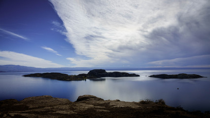 Small rocky island in front of the village of Chiloe. This island is located in the General Carrera Lake in Patagonia, Chile. The background is full of mountains and clouds.
