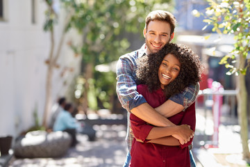 Diverse young couple hugging while standing together on a sidewalk - Powered by Adobe