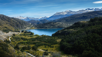 Fototapeta na wymiar Characteristic landscape of the Andes mountain range in Argentine or Chilean Patagonia. There is a beautiful lake, a forest, great mountains and a dirt road.
