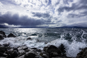 Fototapeta premium Lake Nahuel Huapi chopped, furious breaking against the coast. Cloudy day, the sun rises. Bariloche, Argentine Patagonia