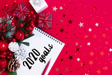 Fototapeta na wymiar 2020 new year xmas goal, plan, action text on notepad with pen, star confetti, red, black gift boxes, christmas decor on red backdrop. Motivation, inspiration concept idea, design flat lay, copy space