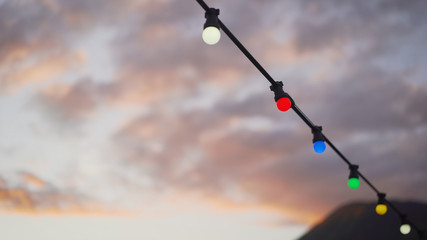 Garland on a background of sunset and mountains. Elements of the beach wedding decoration, parties. Lamps and hearts hung on a rope against the sea.