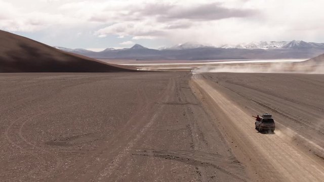 Driving down DRONE shot of car in desert on Bolivia's Salt Flats. DRONE Shot of couple in Salar de Uyuni salt flat. Dry landscape, empty. Holiday, vacation, driving, roadtrip, journey, long road
