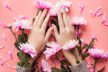 Hands of a girl with a gentle manicure in flowers on a pink background. The concept of caring for the skin of hands in winter. Thin hands of a girl on a pastel background with chrysanthemums.