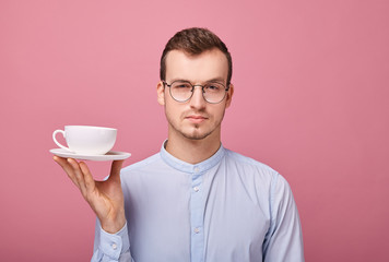 A guy in a blue shirt with glasses and a black rim is resting with a white mug of coffee in his...
