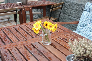 a bouquet of cut sunflowers and placed in a glass vase on a wooden table wet with rain in the fall