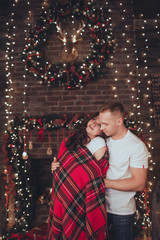 Lovely couple woman and man are covered in blanket at home near fireplace. Christmas time.