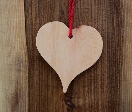 Braunes Herz aus Holz an roter Schnur auf einer Holzwand, Hintergrund, Motiv Postkarte