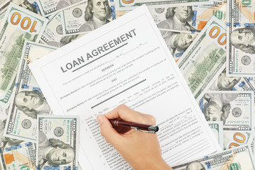 A woman reads and signs a loan agreement on the background of dollar bills. Concept of loan, mortgage, installment. Top view.