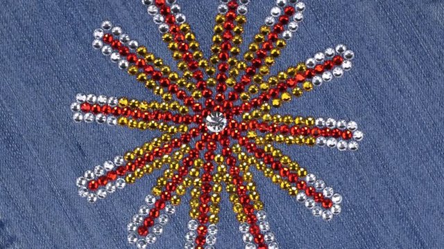 Rotation of multi-colored rhinestones laid out in the shape of a star on denim.
